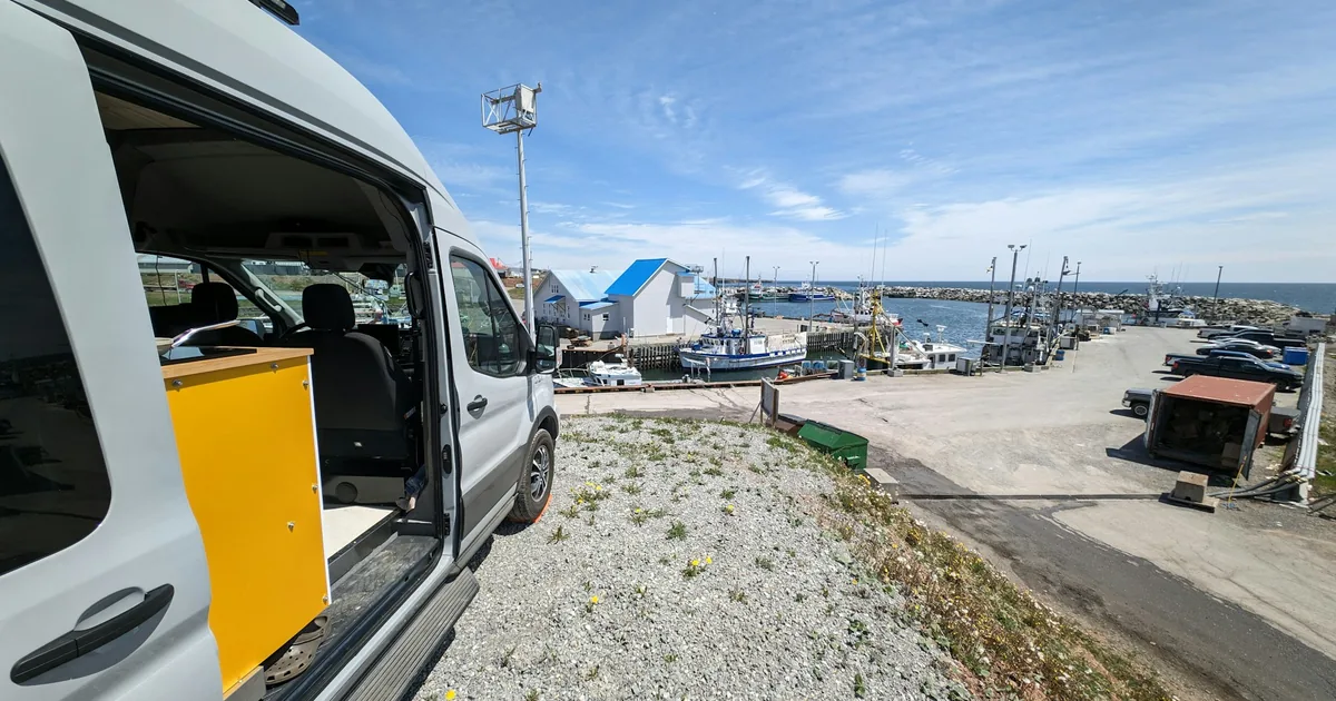 Bobil parkert ved en havn med fiskebåter i bakgrunnen